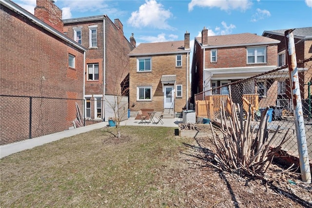 rear view of property with brick siding, entry steps, a fenced backyard, a yard, and a patio