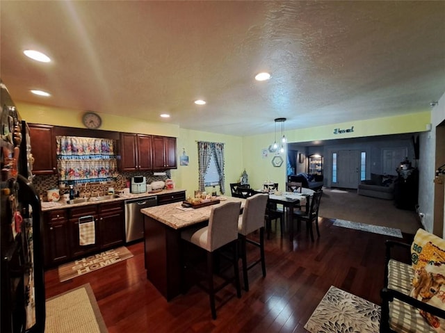 kitchen with backsplash, dark wood-type flooring, a kitchen bar, light countertops, and stainless steel dishwasher