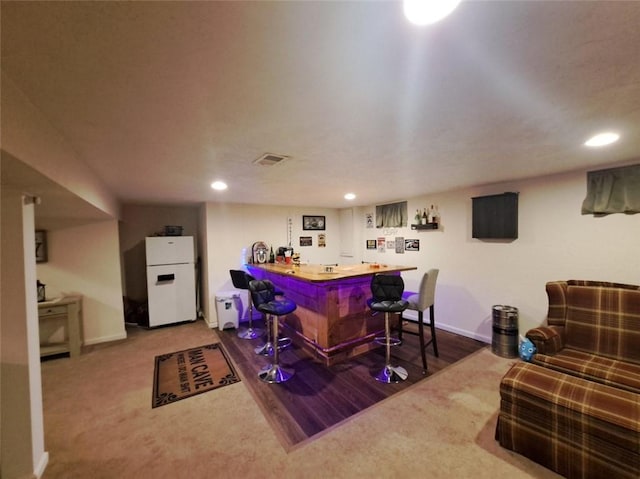 bar featuring visible vents, a bar, freestanding refrigerator, and baseboards