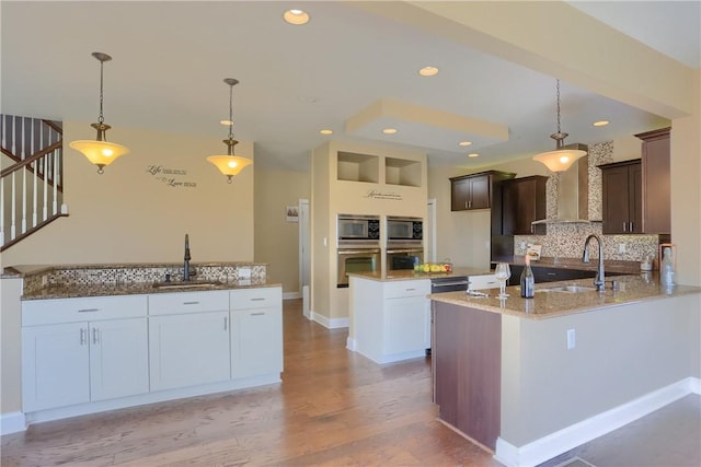 kitchen with backsplash, light stone countertops, wall chimney exhaust hood, and a sink