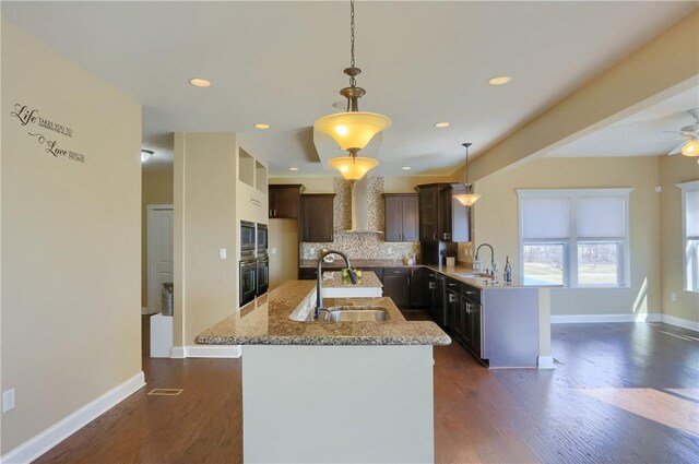 kitchen with backsplash, wall chimney range hood, dark wood finished floors, a peninsula, and a sink