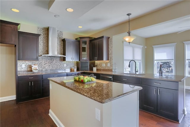 kitchen featuring stone counters, a peninsula, a sink, stainless steel dishwasher, and wall chimney exhaust hood