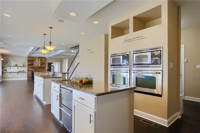 kitchen featuring a kitchen island with sink, open floor plan, dark stone counters, appliances with stainless steel finishes, and dark wood-style flooring