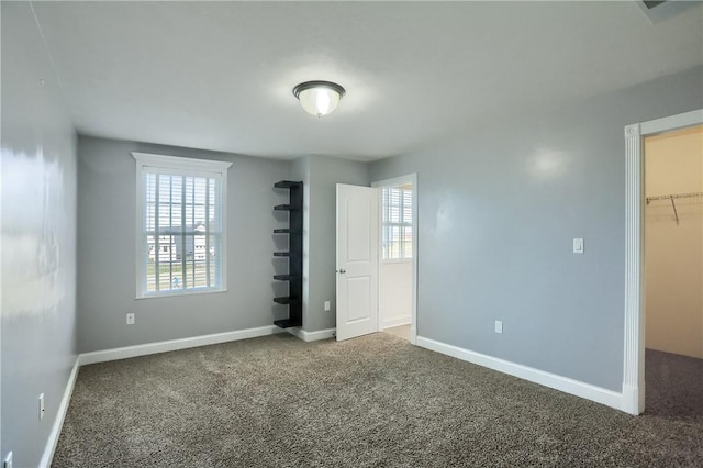 unfurnished bedroom with multiple windows, carpet floors, baseboards, and a spacious closet