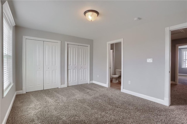 unfurnished bedroom featuring connected bathroom, baseboards, two closets, and carpet flooring