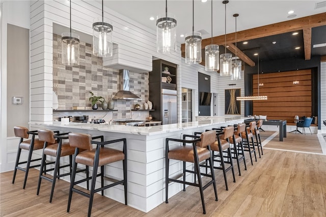 kitchen featuring wall chimney range hood, light wood-style flooring, tasteful backsplash, and stainless steel built in refrigerator