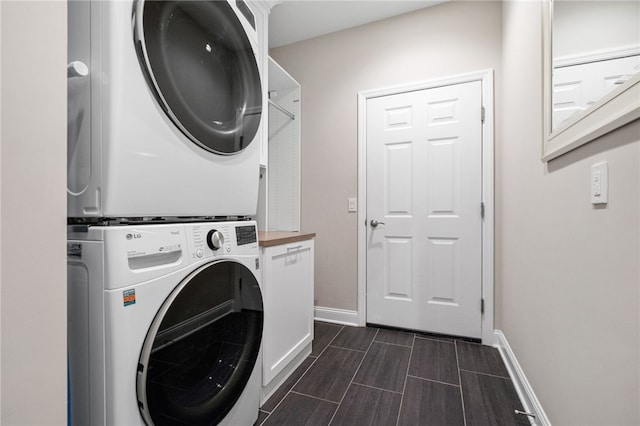 laundry room featuring stacked washer / dryer, cabinet space, baseboards, and wood tiled floor