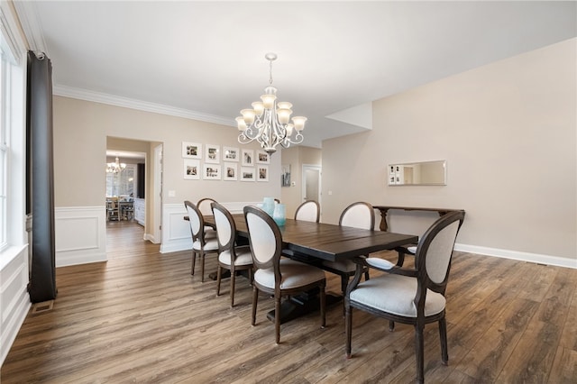 dining space with wood finished floors, wainscoting, crown molding, a decorative wall, and a notable chandelier