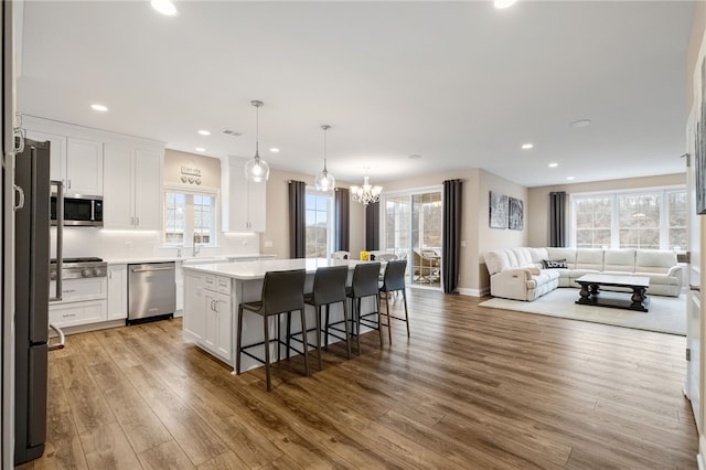 kitchen with wood finished floors, open floor plan, a center island, appliances with stainless steel finishes, and white cabinets