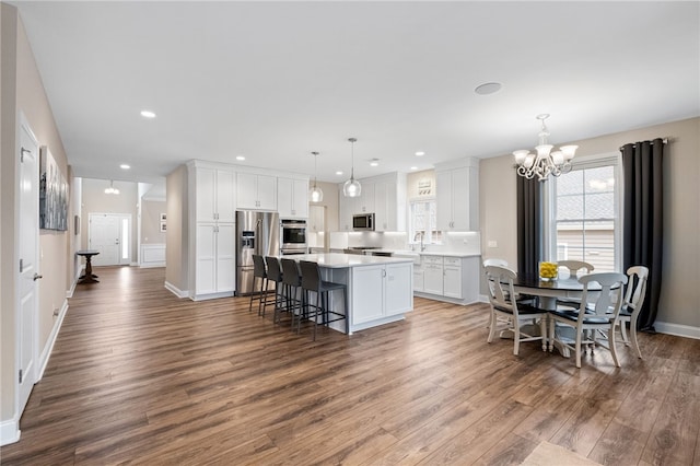 kitchen featuring wood finished floors, light countertops, appliances with stainless steel finishes, white cabinetry, and a center island