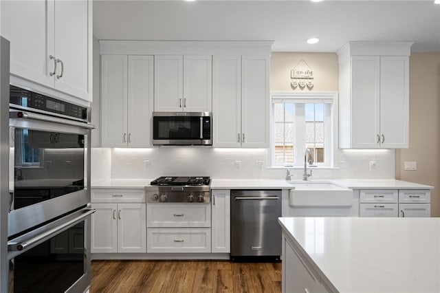 kitchen featuring dark wood finished floors, a sink, decorative backsplash, stainless steel appliances, and white cabinets