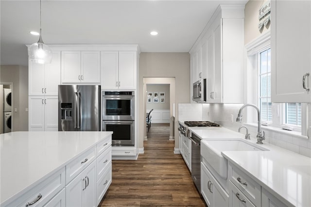 kitchen with stacked washing maching and dryer, dark wood finished floors, light countertops, appliances with stainless steel finishes, and tasteful backsplash