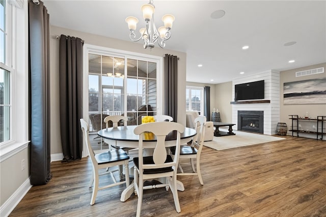 dining room with wood finished floors, visible vents, a large fireplace, and a chandelier