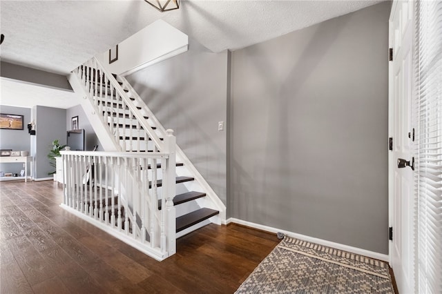 stairs with wood finished floors, baseboards, and a textured ceiling