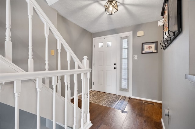 foyer entrance featuring visible vents, a textured ceiling, wood finished floors, baseboards, and stairs