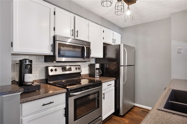 kitchen featuring tasteful backsplash, white cabinets, appliances with stainless steel finishes, and dark wood-style flooring