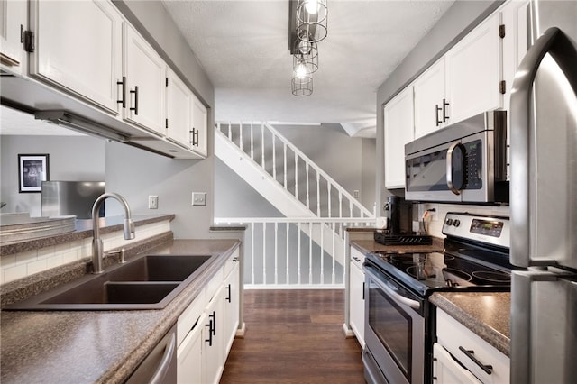 kitchen with dark wood-type flooring, dark countertops, appliances with stainless steel finishes, and a sink