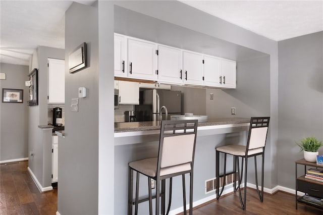 kitchen featuring dark wood-style floors, a breakfast bar area, white cabinetry, and stainless steel appliances