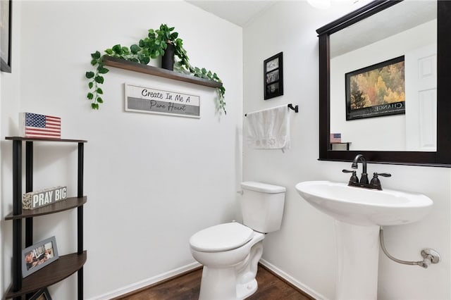 half bathroom featuring toilet, wood finished floors, baseboards, and a sink