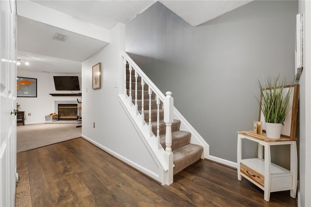 stairs featuring a glass covered fireplace, visible vents, baseboards, and wood finished floors