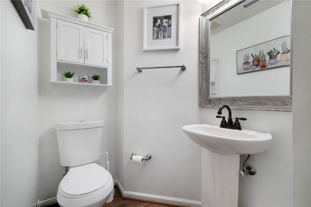 half bathroom featuring toilet, baseboards, visible vents, and a sink