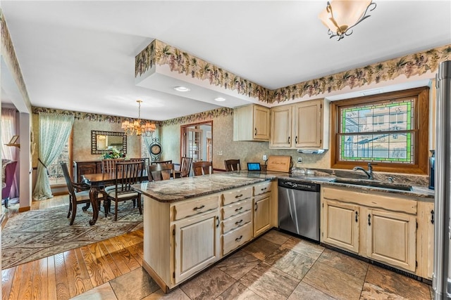 kitchen featuring wallpapered walls, a peninsula, dark stone counters, a sink, and dishwasher