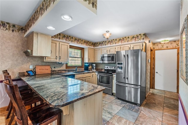 kitchen featuring wallpapered walls, a peninsula, a sink, appliances with stainless steel finishes, and a kitchen bar