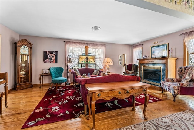 living room with a fireplace, wood finished floors, visible vents, and baseboards