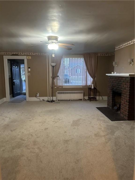 unfurnished living room featuring a brick fireplace, radiator, carpet, and ceiling fan