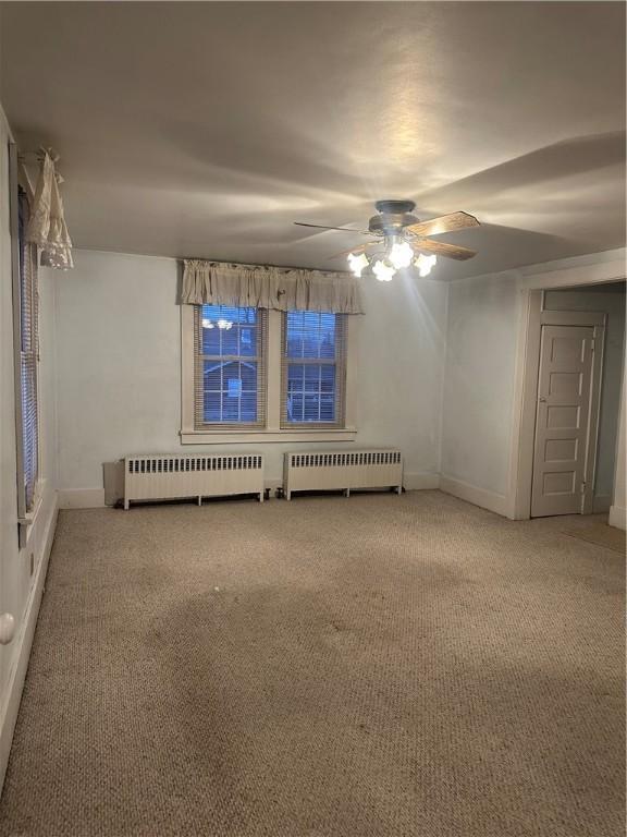 empty room featuring carpet floors, radiator, and a ceiling fan