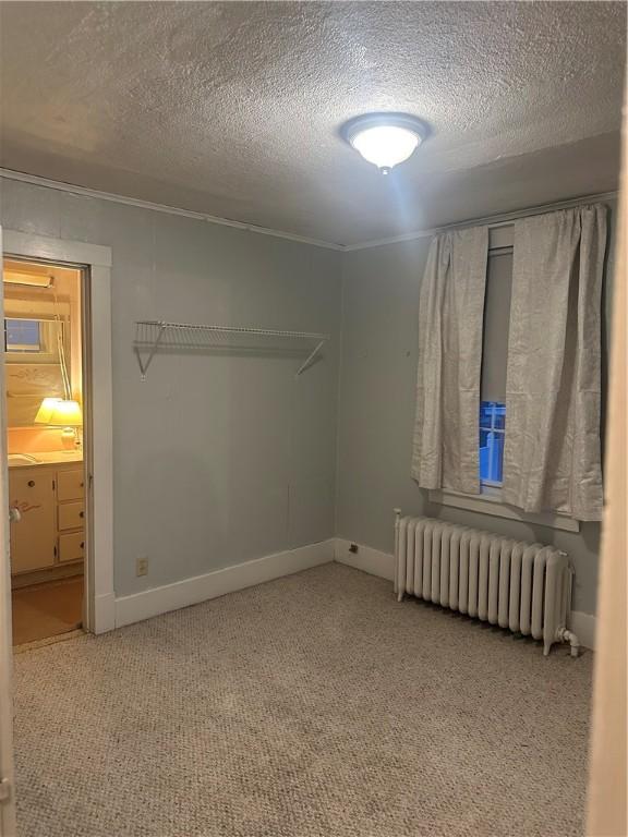 unfurnished bedroom with carpet flooring, radiator, a textured ceiling, and baseboards