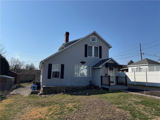 rear view of property featuring a chimney, a yard, and fence