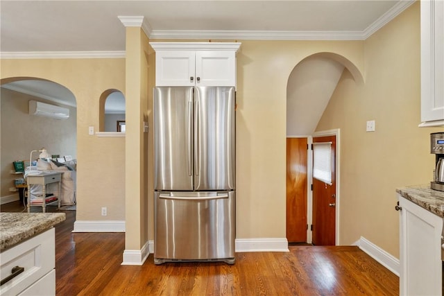 kitchen featuring light stone countertops, an AC wall unit, freestanding refrigerator, dark wood-style floors, and white cabinetry