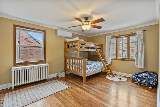 bedroom with a wall mounted air conditioner, radiator heating unit, baseboards, and wood finished floors