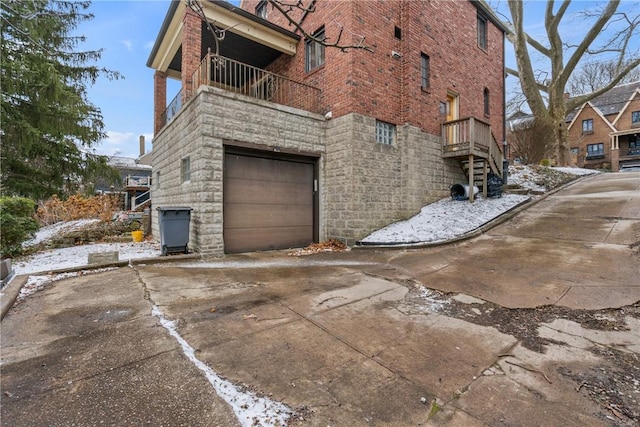 view of home's exterior with brick siding, concrete driveway, a balcony, a garage, and stone siding