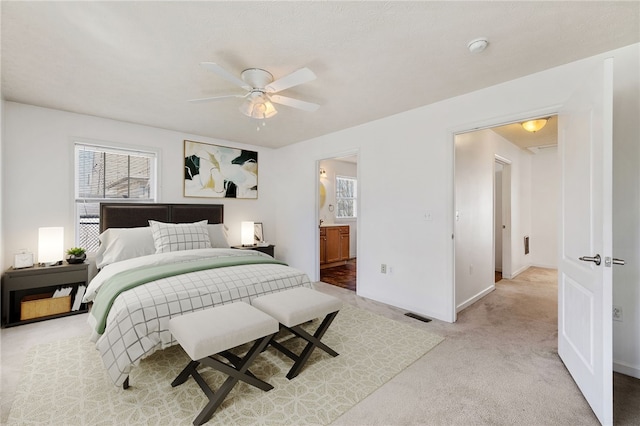 bedroom featuring visible vents, light carpet, ensuite bathroom, baseboards, and ceiling fan