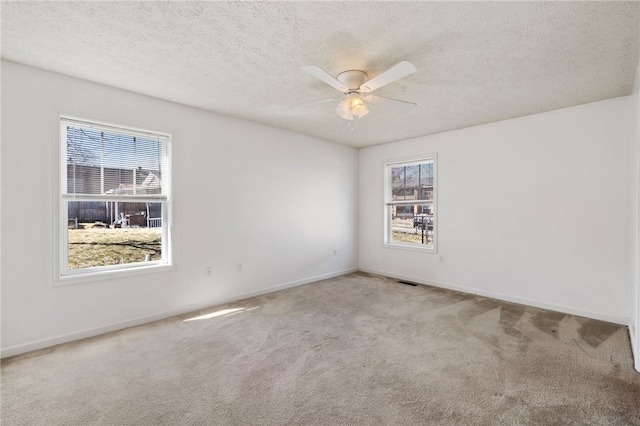 carpeted empty room featuring baseboards, visible vents, a textured ceiling, and ceiling fan