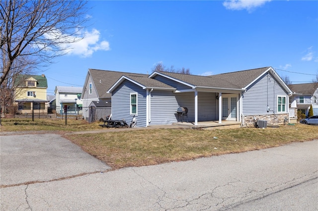 view of front facade with a front lawn, stone siding, a porch, fence, and roof with shingles