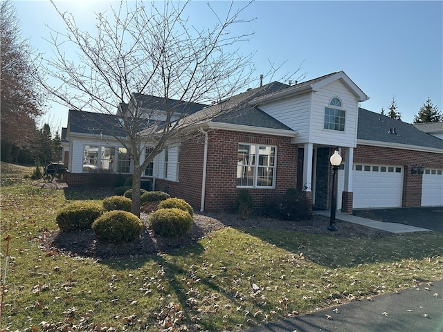 traditional-style house featuring driveway, a front lawn, roof with shingles, an attached garage, and brick siding