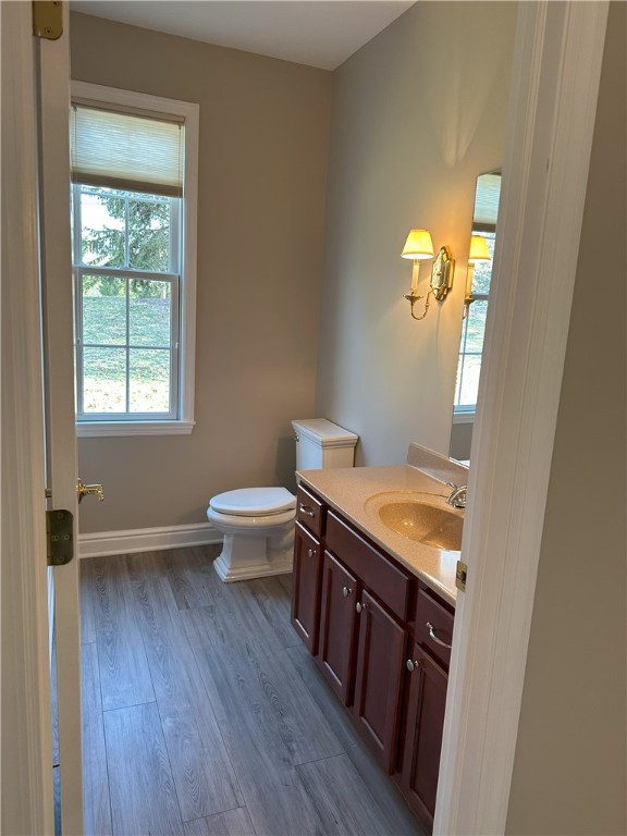 half bath featuring vanity, toilet, wood finished floors, and baseboards