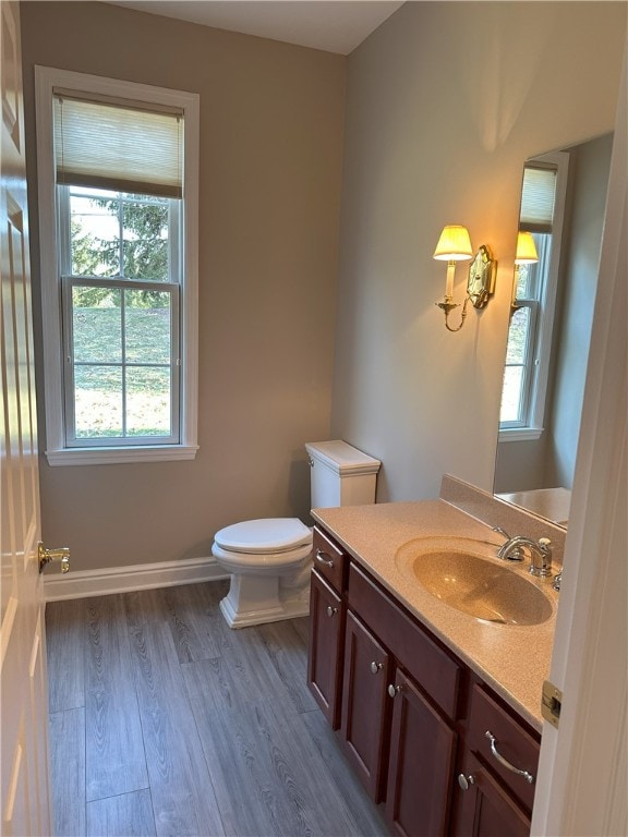 half bathroom with vanity, toilet, wood finished floors, and baseboards