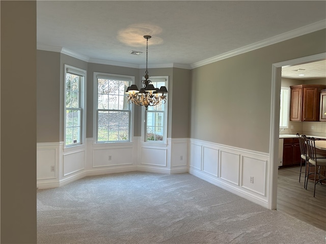 unfurnished dining area featuring visible vents, wainscoting, crown molding, a notable chandelier, and light colored carpet