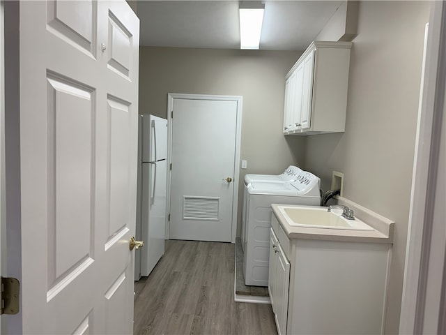 laundry room featuring light wood-type flooring, visible vents, a sink, cabinet space, and washing machine and clothes dryer