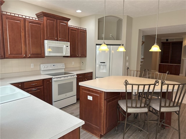 kitchen featuring white appliances, a breakfast bar, tasteful backsplash, light wood-type flooring, and a center island