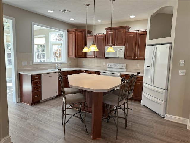 kitchen with a kitchen bar, white appliances, light wood-style flooring, and light countertops