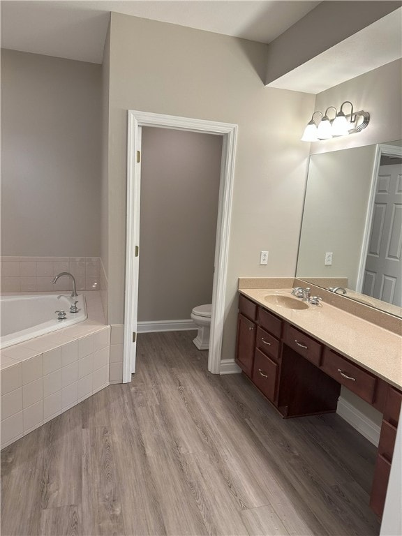 bathroom with a garden tub, toilet, wood finished floors, baseboards, and vanity