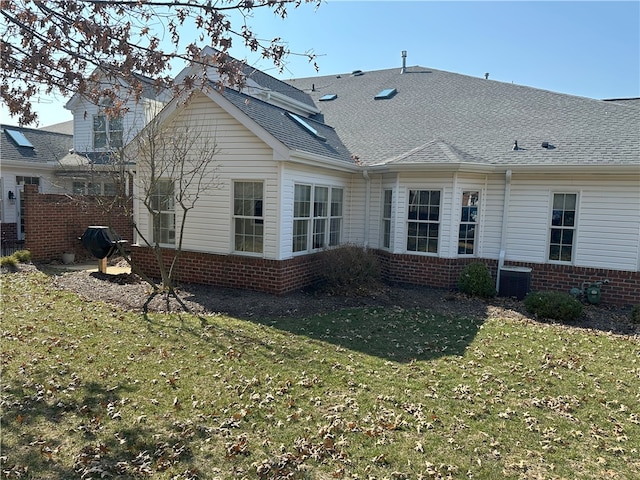 back of house featuring brick siding, a lawn, central AC, and roof with shingles