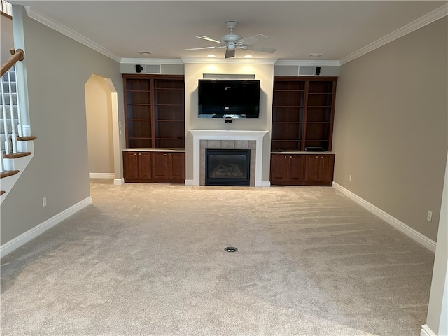 unfurnished living room featuring stairs, arched walkways, a tiled fireplace, and crown molding