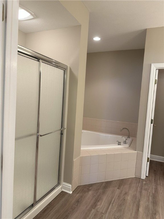 bathroom featuring wood finished floors, a bath, and a shower stall