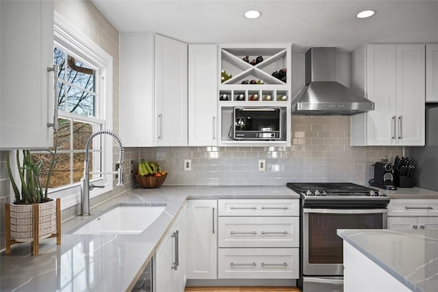 kitchen with decorative backsplash, stainless steel gas stove, white cabinets, wall chimney exhaust hood, and a sink